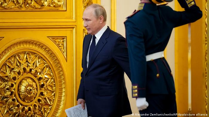 Russlands Präsident Wladimir Putin geht durch eine goldene Tür im Kreml, ein Wachmann salutiert