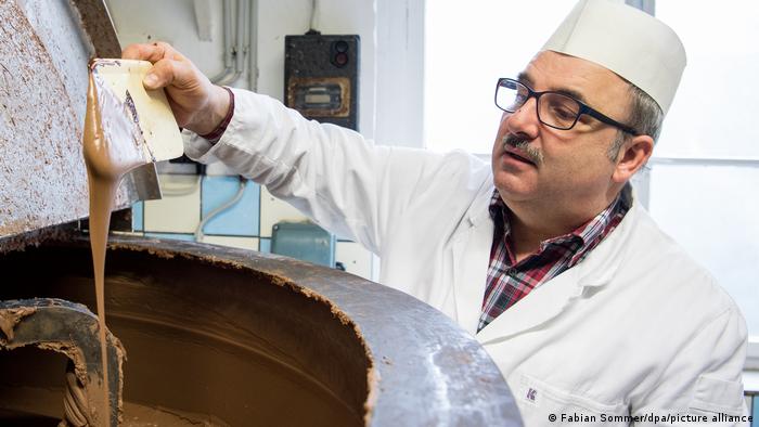 Blick in den Schokoladenkessel in einer Schokoladenfabrik. Ein Mann prüft die Konsistenz der Schokolade. 