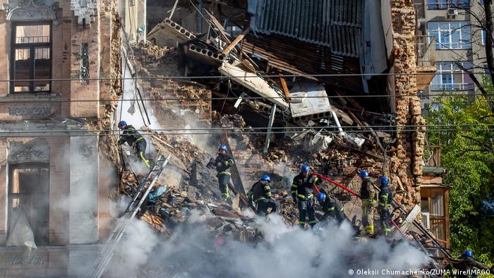 Ukraine Krieg | Angriff russische Drohnen in Kiew. Ein Haus ist von einer Drohne getroffen und zerstört worden. Die Aufnahme wurde am 17. Oktober gemacht. Feuerwehrleute stehen im Schutt, im Vordergrund ist Rauch zu sehen.