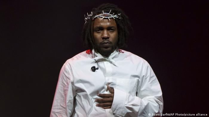 Kendrick Lamar steht in weißem Hemd und mit Dornenkranz auf dem Kopf vor einem schwarzen Hintergrund