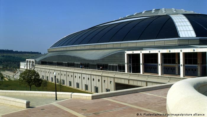 Außenansicht der Arena Palau Sant Jordi: Zu sehen ist ein Gebäude mit einem rundlichen Dach und geschwungenen Seiten. 