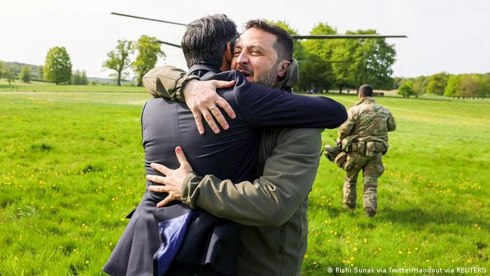 Der britische Premierminister Rishi Sunak und der ukrainische Präsident Wolodymyr Selenskyj umarmen sich auf einer grünen Wiese