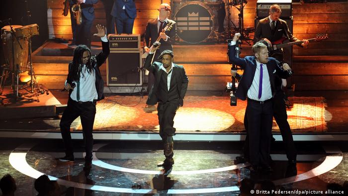 Seeed auf der Bühne, vorne tanzen die drei Sänger.