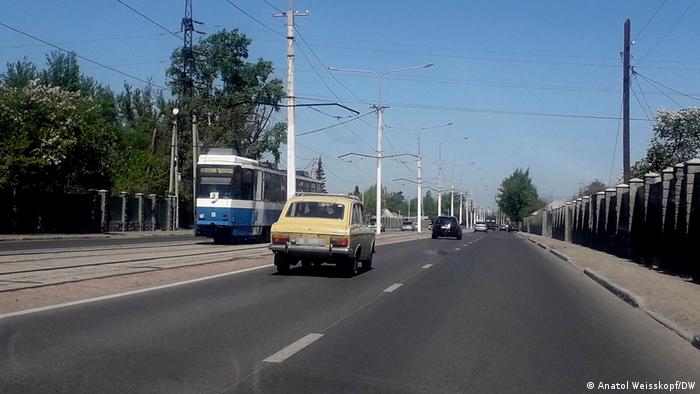 Ein Auto auf einer Straße in Ust-Kamenogorsk, die in Richtung Russland führt. Eine Straßenbahn kommt entgegen, im Hintergrund fahren weitere Autos